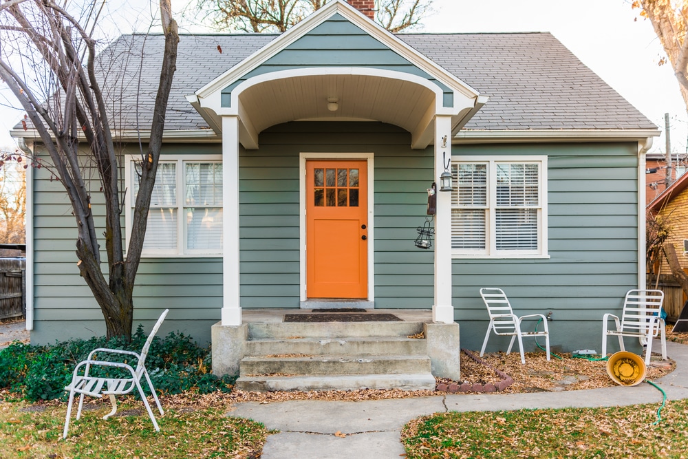 The front of a small house with a green exterior and a bright orange front door
