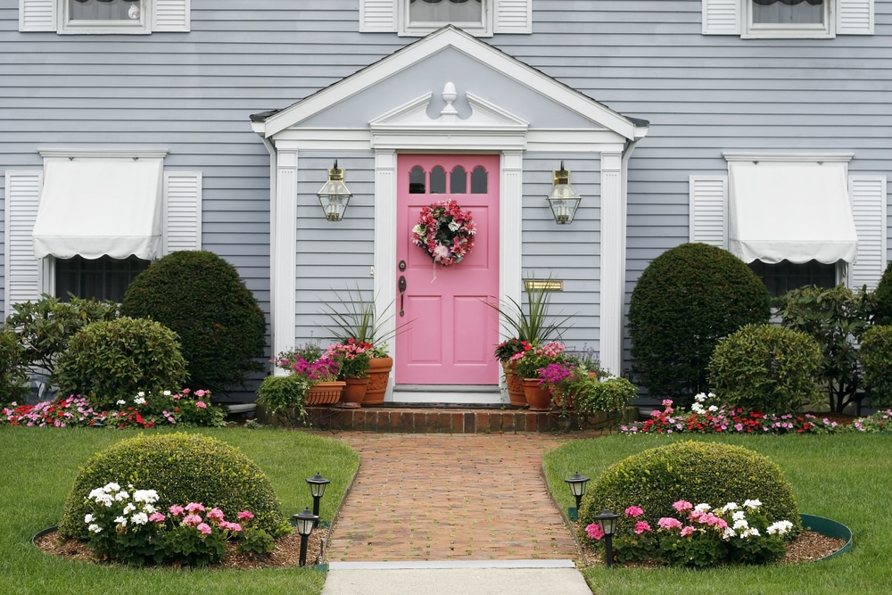 The front of a light blue home with a bright pink front door and wreath