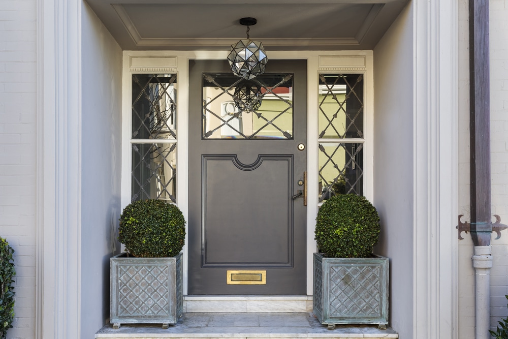 A gray front door with a gold mail slot and potted bushes on either side