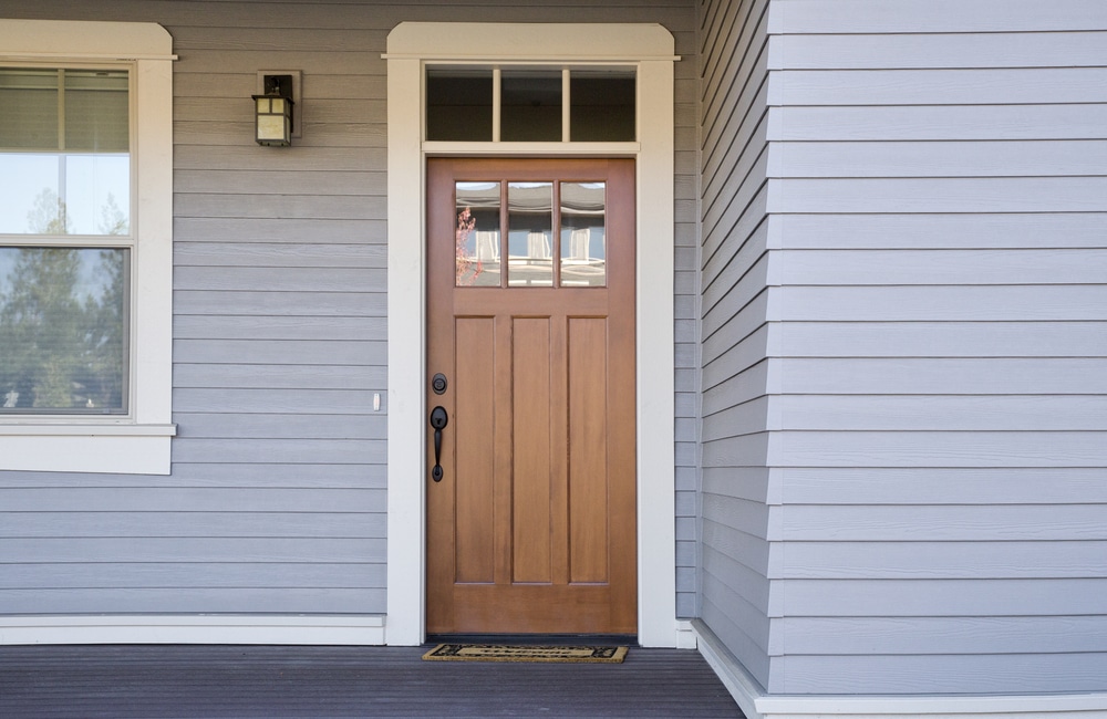 A natural wood front door with white exterior molding and black hardware
